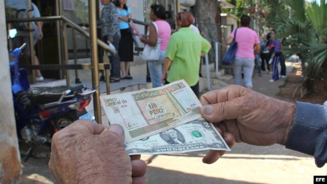 Un hombre muestra un peso convertible cubano y un dólar estadounidense frente a una oficina de Western Union en La Habana (Cuba).
