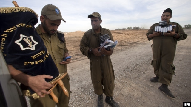 Soldado israelíes cargan con una Torá y libros de rezo mientras otros soldados se preparan para desplegarse junto a la frontera con Gaza, en Israel. 