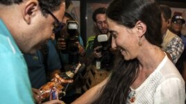 La disidente cubana Yoani Sánchez (d), autora del blog "Generación Y", recibe del cineasta Dado Galvao (i), su anfitrión en Brasil, una cinta de "Senhor do Bonfim" hoy, lunes 18 de febrero de 2013, en el aeropuerto internacional Guararapes, de la ciudad d