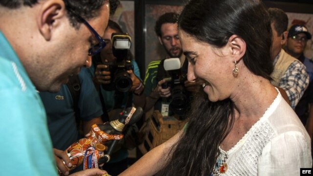 La disidente cubana Yoani Sánchez (d), autora del blog "Generación Y", recibe del cineasta Dado Galvao (i), su anfitrión en Brasil, una cinta de "Senhor do Bonfim" hoy, lunes 18 de febrero de 2013, en el aeropuerto internacional Guararapes, de la ciudad d