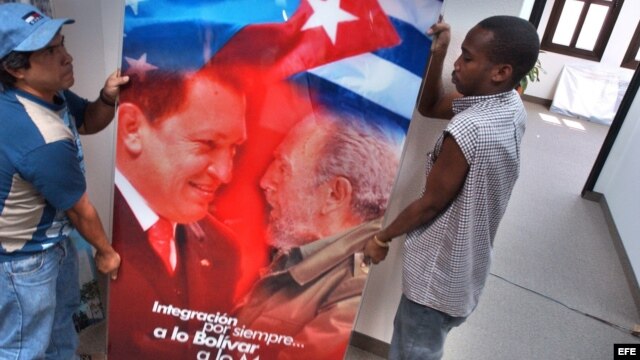 Dos obreros trasladan un cristal con la imagen de Hugo Chávez y Fidel Castro.