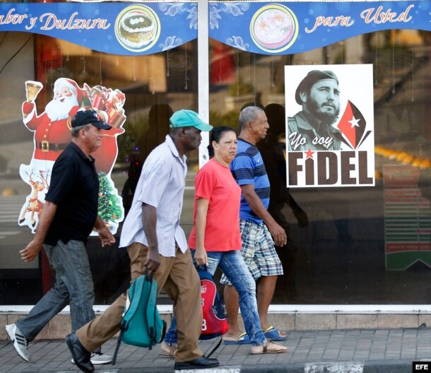 Varias personas camina por una calle en Santiago de Cuba, junto a imagen del líder de la revolución cubana Fidel Castro