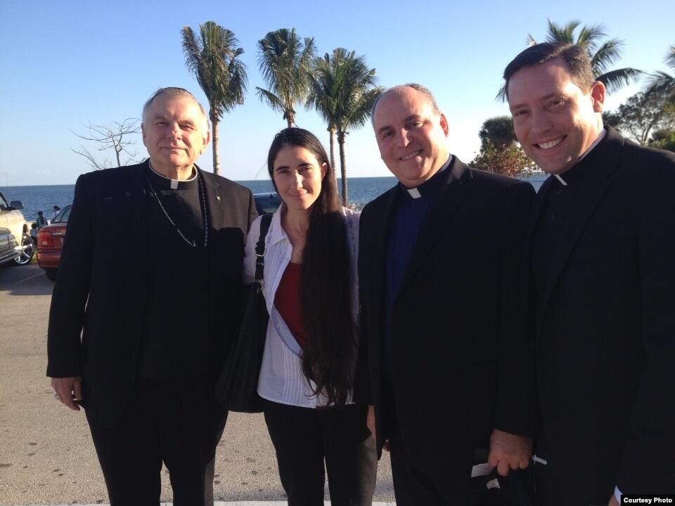 Yoani Sánchez en la Ermita de la Caridad, entre el arzobispo Thomas Wenski, a la izquierda, y el párroco Juan Rumín Domíguez, a la derecha. 