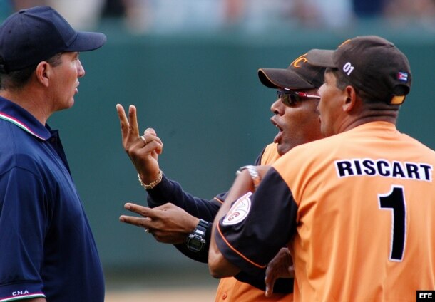 El director técnico de Villa Clara, Víctor Mesa (c) es aguantado por el entrenador de pitcheo de su equipo, José Ramón Riscart (d) mientras discute con el árbitro principal Pedro Morgado (i.) durante un partido en el estadio Latinoamericano.