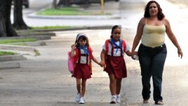 Dos niñas son llevadas por su madre hacia la escuela.