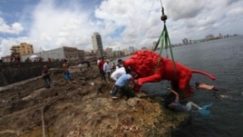 El artista plástico cubano Roberto Favelo (i) posa junto a un león rojo creado por él que conforma la obra "Garras en la piedra"  que se instala en los arrecifes del malecón de La Habana (Cuba). Esta pieza forma parte de la exposición colectiva "Detrás de