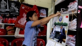 Una mujer de la Liga Nacional por la Democracia (NLD) cuelga un calendario con la fotografía de la opositora birmana Aung San Suu Kyi y el presidente de Estados Unidos en la tienda de recuerdos del partido en Rangún (Birmania). 