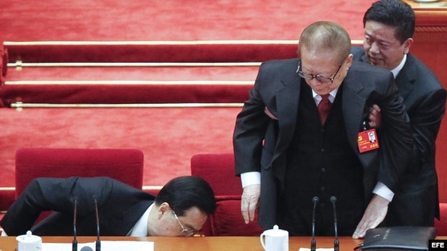 El presidente de China, Hu Jintao (i), guarda sus documentos en un cajón mientras un asistente ayuda a levantarse al expresidente Jiang Zemin tras la clausura del XVIII Congreso del PCCh.