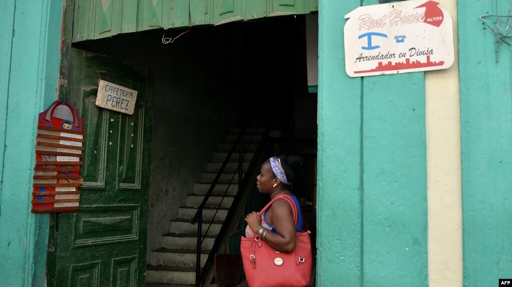 Una mujer parada junto a dos seÃ±ales de negocios privados en Cuba. 