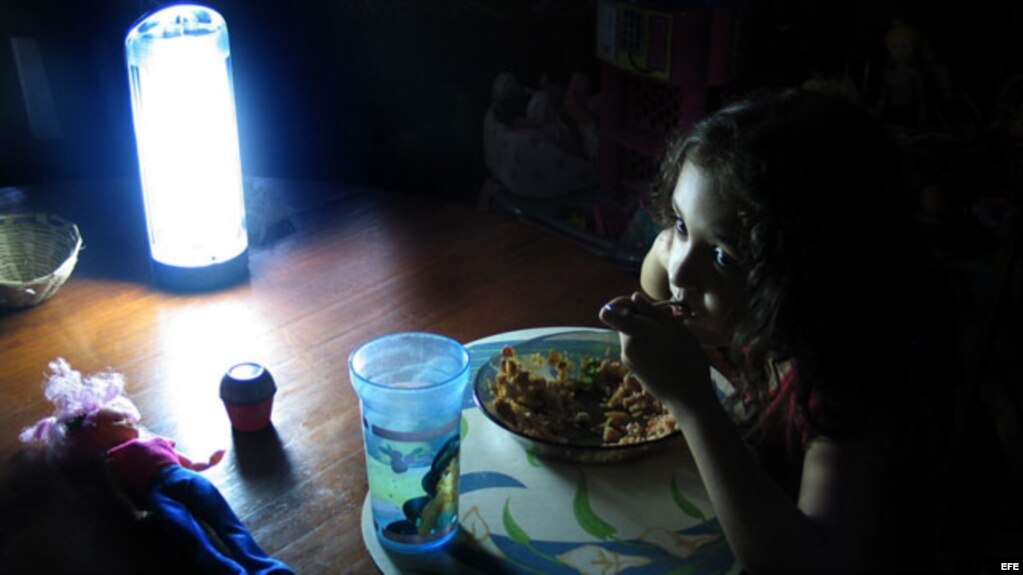 Niña come alumbrada por una lámpara de baterías durante un apagón. (Archivo)